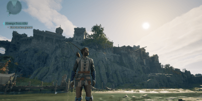 A warrior stands in shallow water, gazing at a grand medieval-style fortress on a rocky hill in Avowed. The sun casts a warm glow over the landscape, highlighting the game's detailed world.