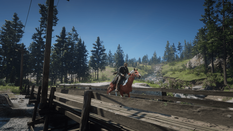 Player character riding a horse across a wooden bridge in a lush forest setting in Red Dead Redemption 2.
